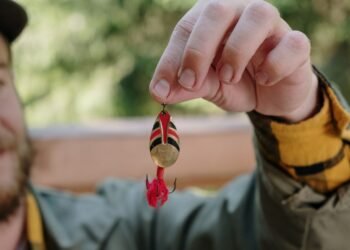 Angler hält einen rot-goldenen Spinner mit Drillingshaken für das Forellenangeln in der Hand.