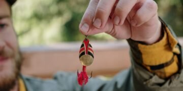 Angler hält einen rot-goldenen Spinner mit Drillingshaken für das Forellenangeln in der Hand.