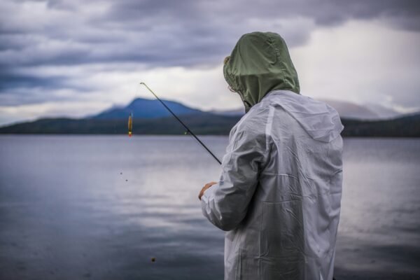 Angler mit wetterfester Kleidung fischt bei Regen an einem norwegischen See und zeigt die wechselhaften Wetterbedingungen in Norwegen.
