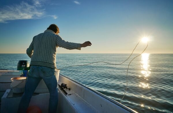 Angler wirft beim Meeresangeln in Norwegen vom Boot seine Angel aus und fischt bei ruhiger See während des Sonnenuntergangs.