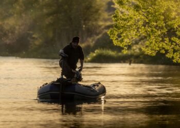 Angler fährt mit einem Schlauchboot und Elektromotor auf einem ruhigen Fluss.