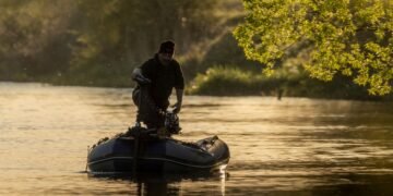 Angler fährt mit einem Schlauchboot und Elektromotor auf einem ruhigen Fluss.
