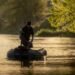 Angler fährt mit einem Schlauchboot und Elektromotor auf einem ruhigen Fluss.