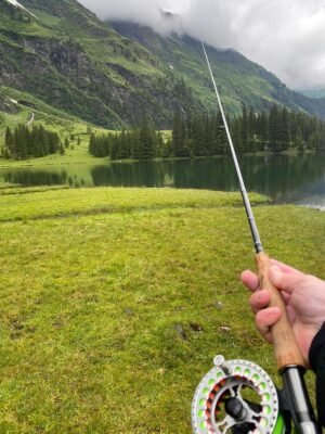 Angler mit Fliegenrute an einem Bergsee in alpiner Landschaft
