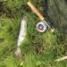 Gefangene Forelle neben Fliegenrute und Fliegenrolle im Gras