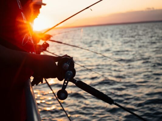 Angler mit Meeresrute und Multirolle beim Angeln vom Boot bei Sonnenuntergang