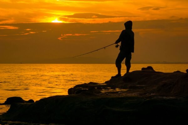 Angler beim Meeresangeln von einer Felsküste bei Sonnenuntergang