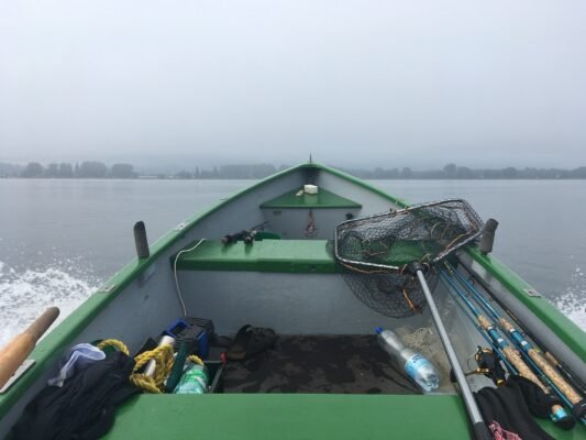Blick aus meinem Angelboot mit Angelruten und Kescher auf dem Wasser