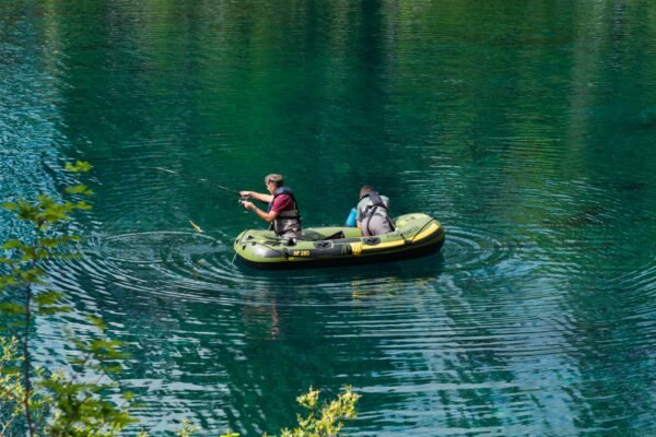Zwei Angler nutzen ein grünes Schlauchboot fürs Angeln auf einem See.
