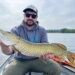 Angler präsentiert einen großen gefangenen Hecht in einem Boot auf dem See