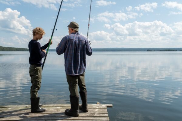 Jugendlicher und erfahrener Angler stehen mit ihren Angelruten auf einem Steg am See