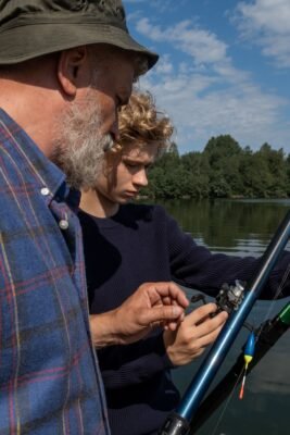 Jugendlicher stellt unter Anleitung eines erfahrenen Anglers eine Angelrolle ein