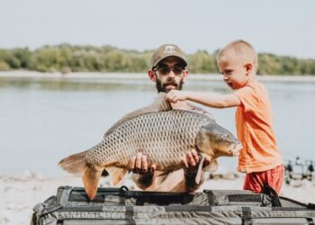 Angler und Kind betrachten einen großen Karpfen am See