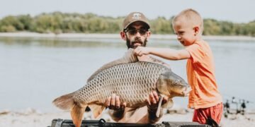 Angler und Kind betrachten einen großen Karpfen am See
