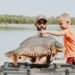 Angler und Kind betrachten einen großen Karpfen am See