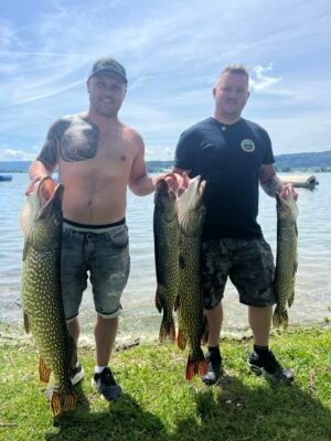 Zwei Angler mit vier großen gefangenen Hechten am Seeufer