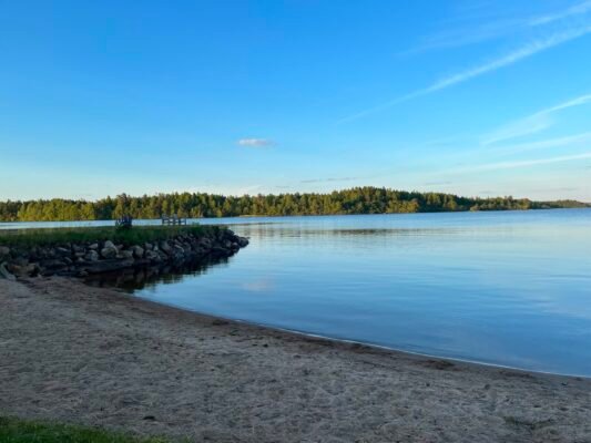 Ruhiger skandinavischer See mit Sandufer und bewaldeter Insel