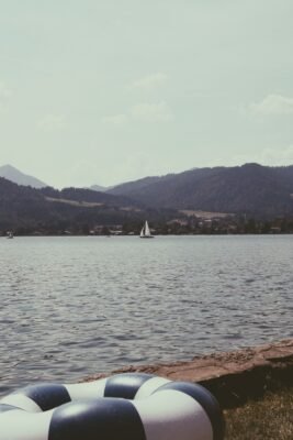 Blick vom Ufer über den Tegernsee mit Segelboot und Bergen im Hintergrund