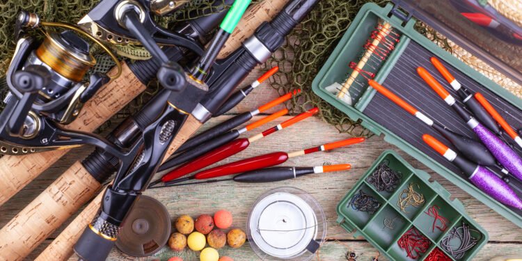 Angelruten mit Rollen, verschiedene Posen, Haken, Schnurspulen und Boilies auf einem Holztisch.