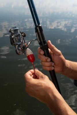 Angler hält eine Welsrute mit Stationärrolle und rot-weißer Pose über dem Wasser