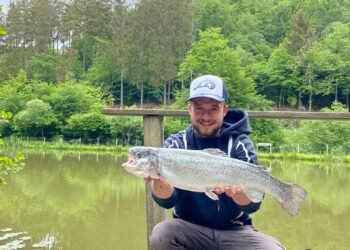 Angler hält eine große Regenbogenforelle auf einem Steg am Forellensee