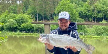 Angler hält eine große Regenbogenforelle auf einem Steg am Forellensee