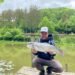 Angler hält eine große Regenbogenforelle auf einem Steg am Forellensee
