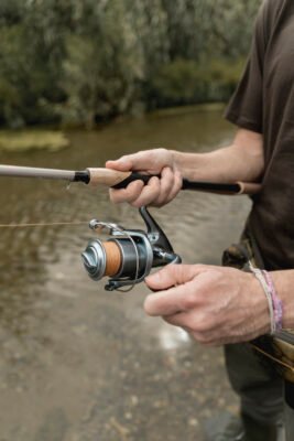 Angler hält eine Rute mit Korkgriff und bedient die Kurbel einer Stationärrolle mit orangefarbener Schnur.