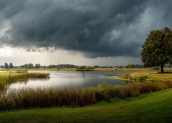 Dunkle Gewitterfront mit Starkregen über einem See und einer Uferlandschaft