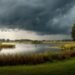 Dunkle Gewitterfront mit Starkregen über einem See und einer Uferlandschaft