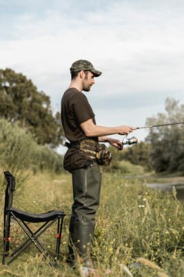 Spinnangler mit körpernah getragener Angeltasche und Angelrute am Flussufer
