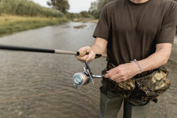 Angler mit Angelrute und Sling Bag beim mobilen Fischen an einem flachen Fluss