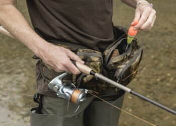 Angler entnimmt einen Schwimmer aus seiner geöffneten Angeltasche am Hüftgurt
