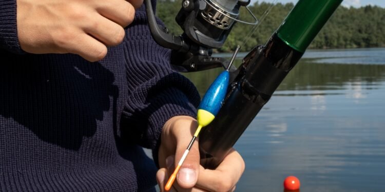 Angler hält eine Angelrute mit Stationärrolle und blau-gelber Pose am See.