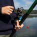 Angler hält eine Angelrute mit Stationärrolle und blau-gelber Pose am See.